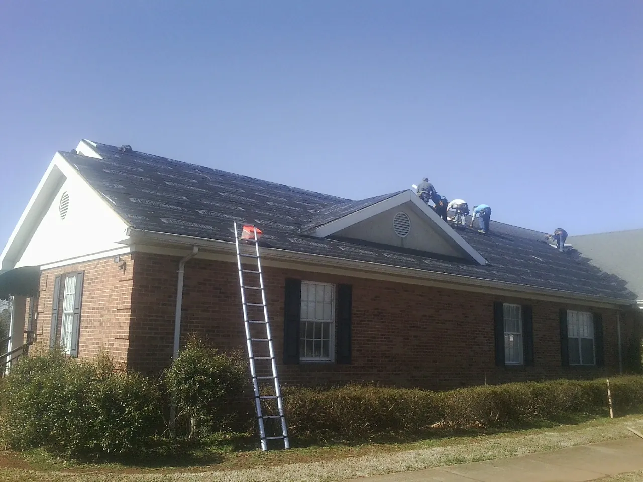 Crew tearing shingles off a brick ranch roof with a ladder set — Emergency Roof Repair work by our crew in Muncie