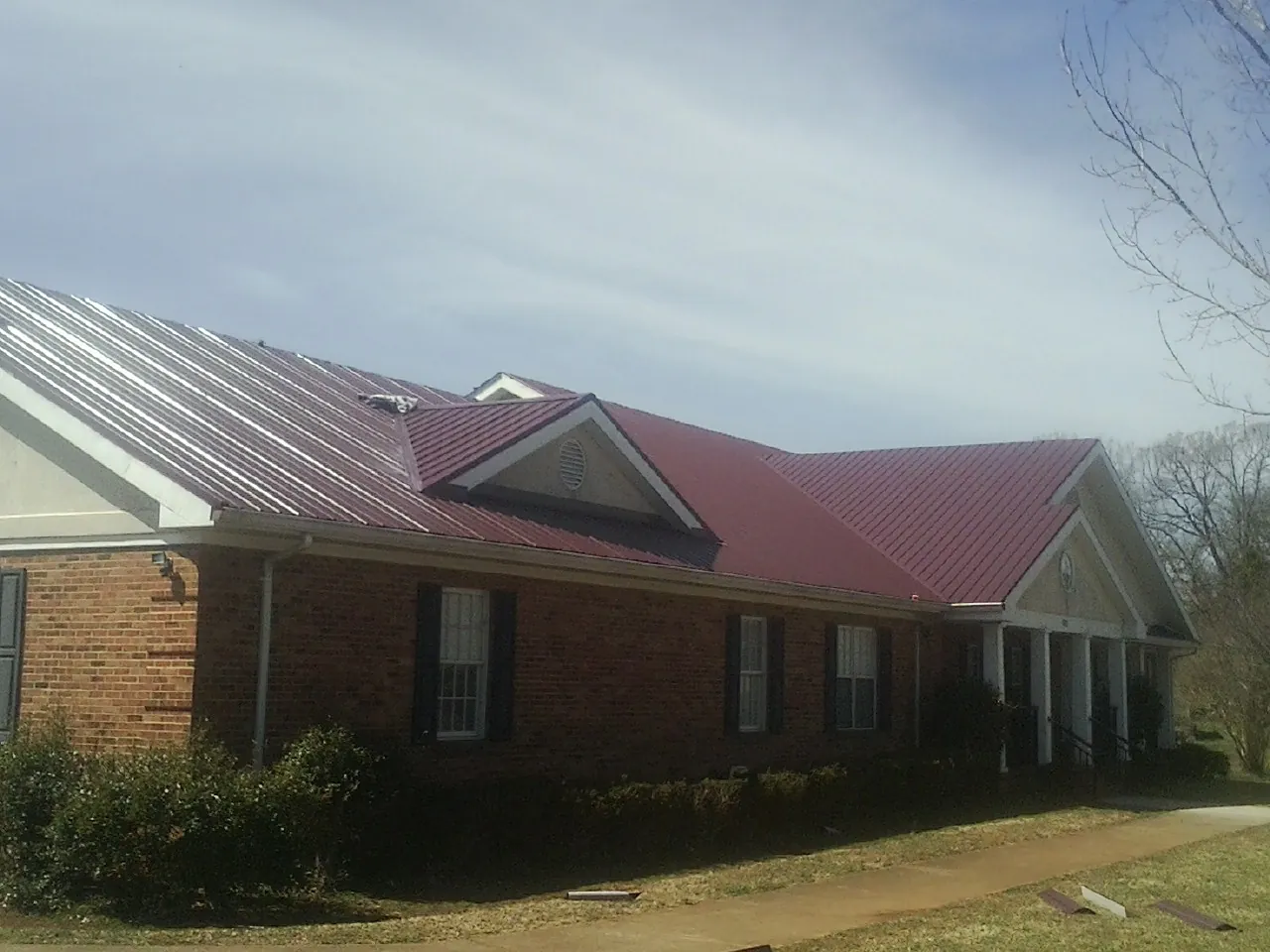 Red metal roof with gabled entries on a long brick building, from a Hail Damage Roof Repair job in Muncie