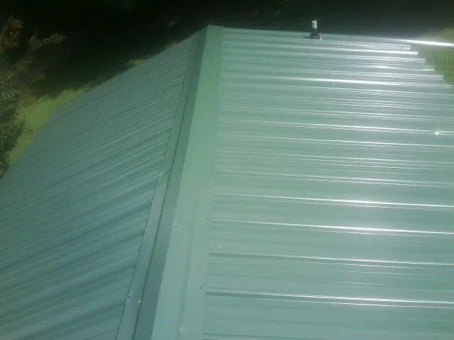 New green metal panels meeting at the ridge of a roof — Flat Roof Repair work by our crew in Muncie