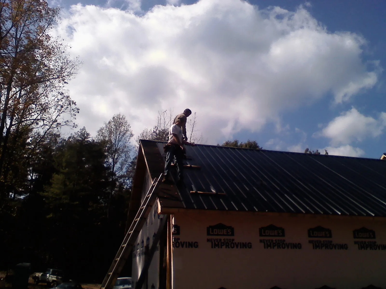 Roofer fastening dark metal panels high against a cloudy sky, from a Roof Inspection job in Muncie