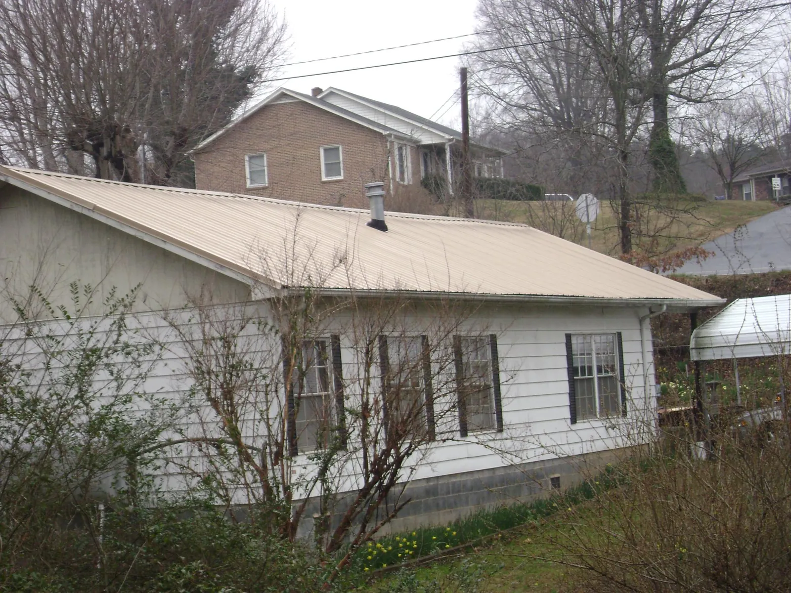 Tan metal roof on a white sided house set into a hillside — Commercial Roofing by Roofing Brothers in Muncie