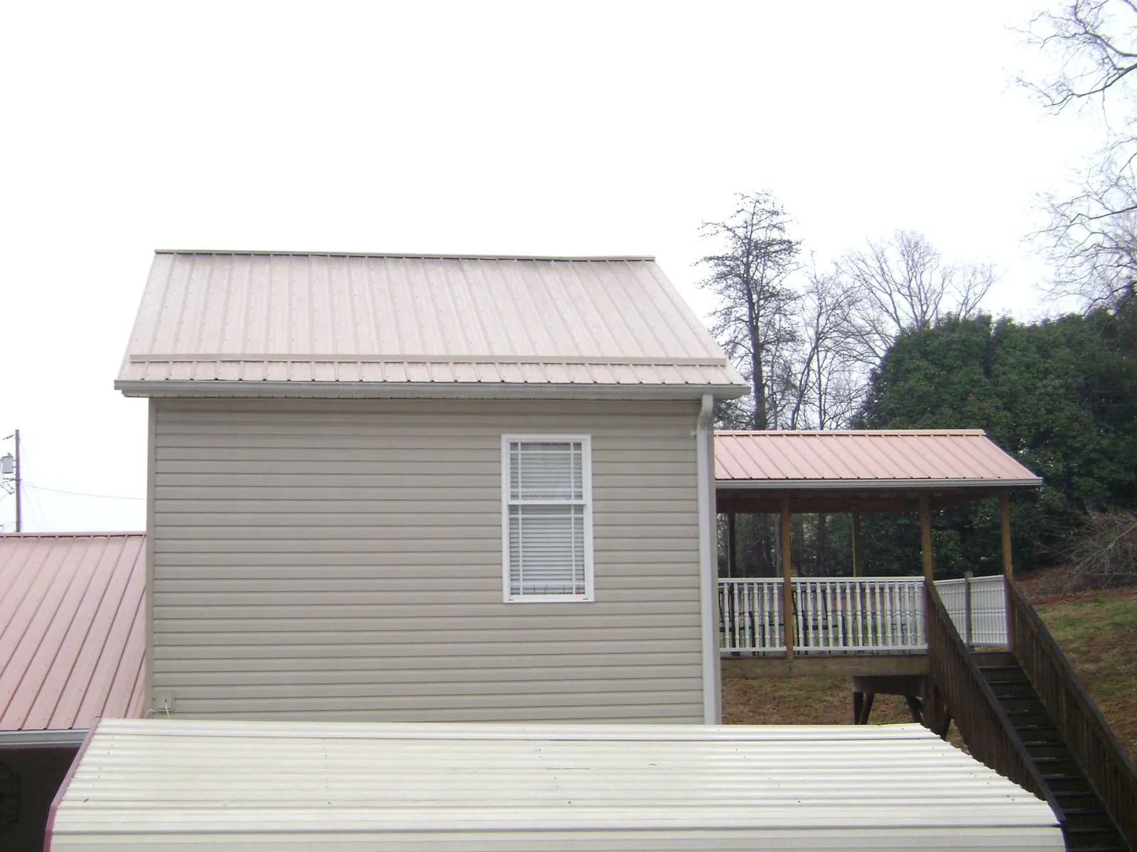 Tan metal roofs on a two story addition and attached porch, from a Roof Replacement job in Muncie